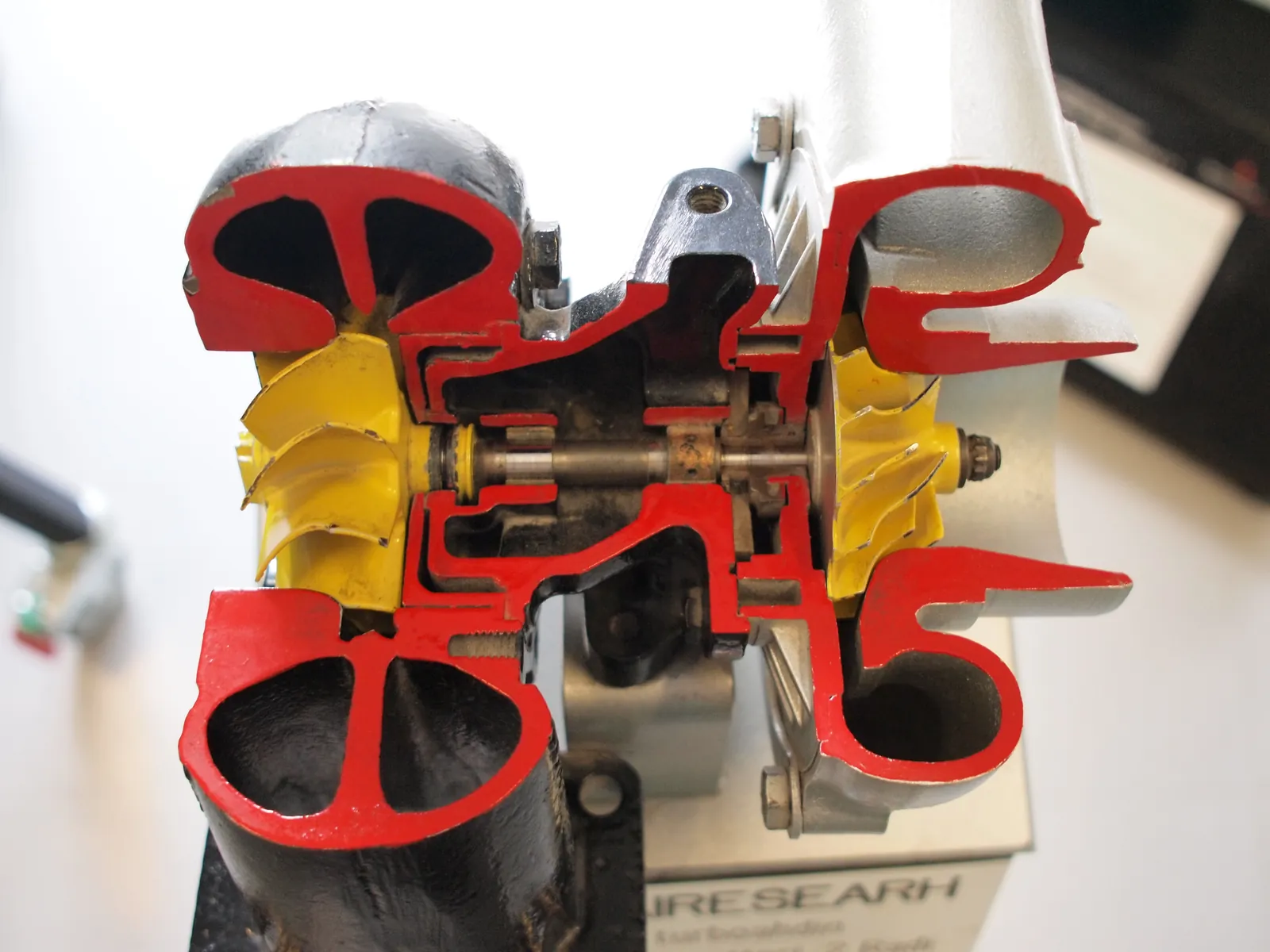 Sectioned Garrett turbocharger, yellow turbine and compressor wheels on one shaft, red-painted cut housings