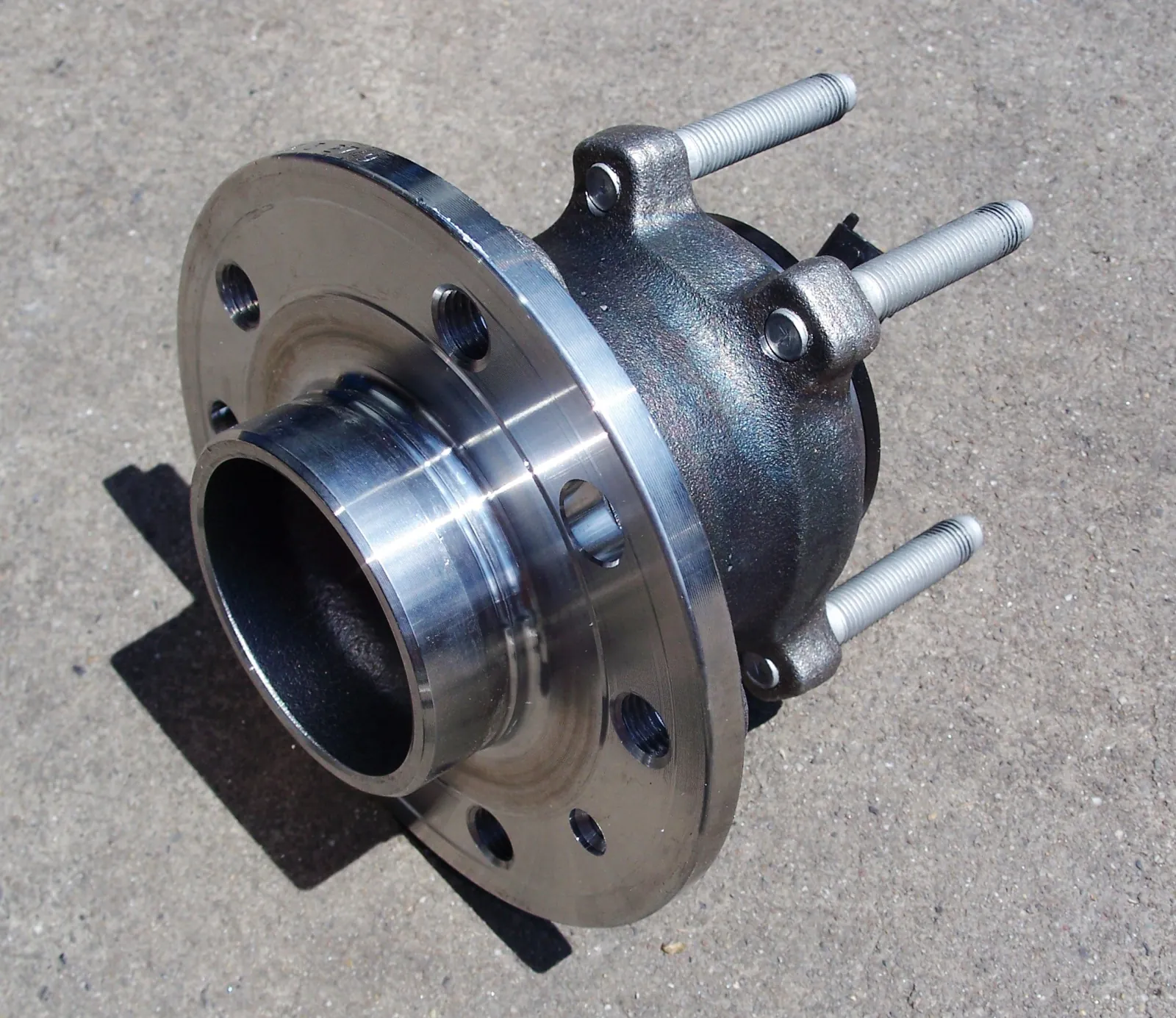 Passenger-car rear wheel hub assembly on concrete, four studs, machined flange, and a sealed bearing in the casting